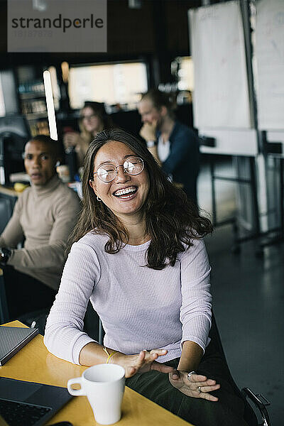 Fröhliche Geschäftsfrau lachend am Schreibtisch eines Start-up-Unternehmens