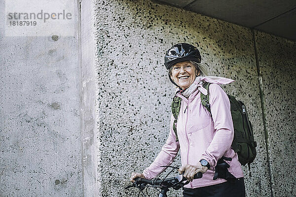 Porträt einer älteren Frau mit Fahrrad an der Wand stehend