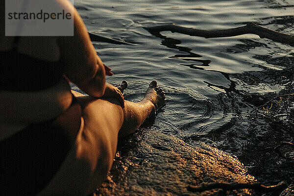 Tiefschnitt einer jungen  üppigen Frau  die bei Sonnenuntergang am Wasser sitzt