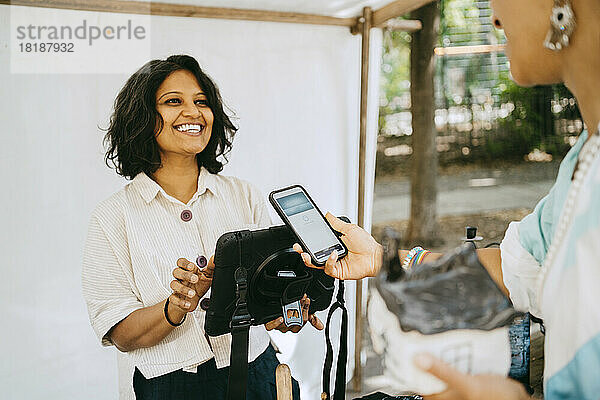 Glückliche Besitzerin im Gespräch mit einem Kunden beim mobilen Bezahlen auf dem Flohmarkt