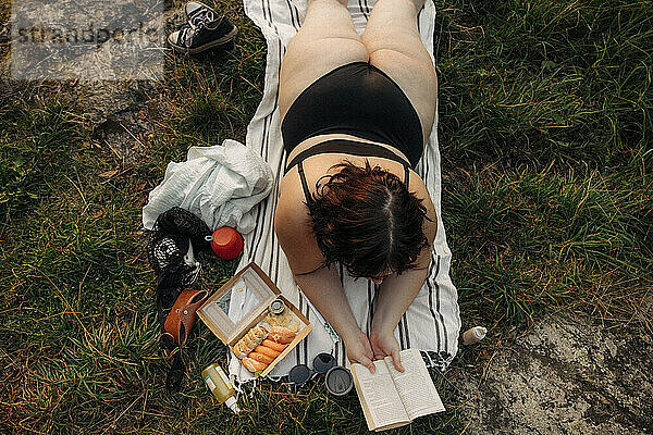 Hohe Winkel Ansicht der üppigen Frau Lesen Buch  während auf Handtuch liegen