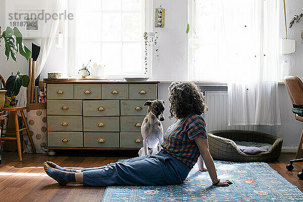 Seitenansicht einer auf dem Boden sitzenden Frau mit Hund zu Hause