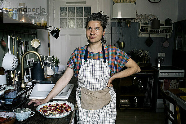 Porträt einer Frau mit Hand auf der Hüfte  die neben einem Kuchen auf der Küchentheke steht