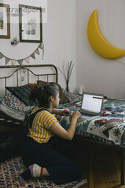 Frau benutzt Laptop  während sie zu Hause neben dem Bett sitzt