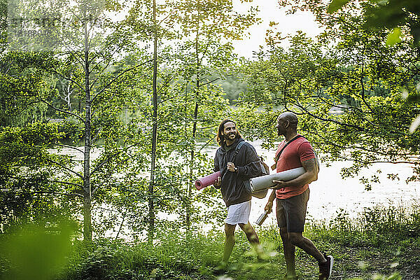 Männliche Freunde tragen Turnmatten und unterhalten sich beim Spaziergang im Wald