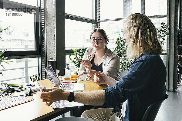 Junge Geschäftsfrau diskutiert am Laptop mit einem Kollegen am Schreibtisch in einem Start-up-Unternehmen