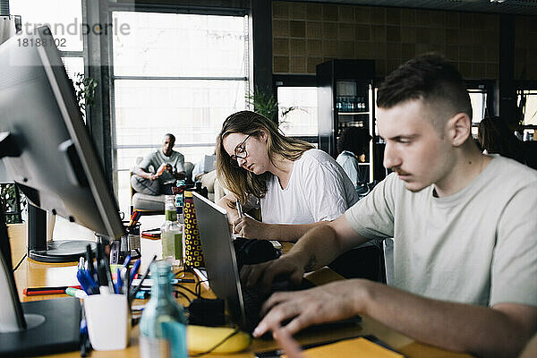 Junger Geschäftsmann arbeitet mit einer Kollegin im Büro am Laptop