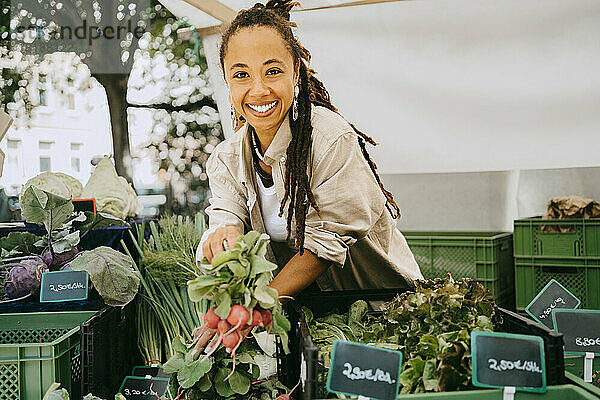 Porträt einer glücklichen Besitzerin mit Gemüse in der Nähe von Kisten an einem Marktstand