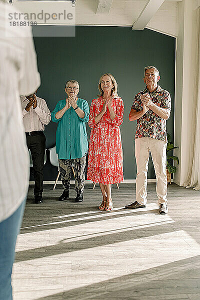 Lächelnde ältere Männer und Frauen klatschen im Stehen beim Tanzunterricht
