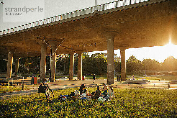 Teenager-Mädchen sitzen auf Gras bei der Brücke im Park bei Sonnenuntergang