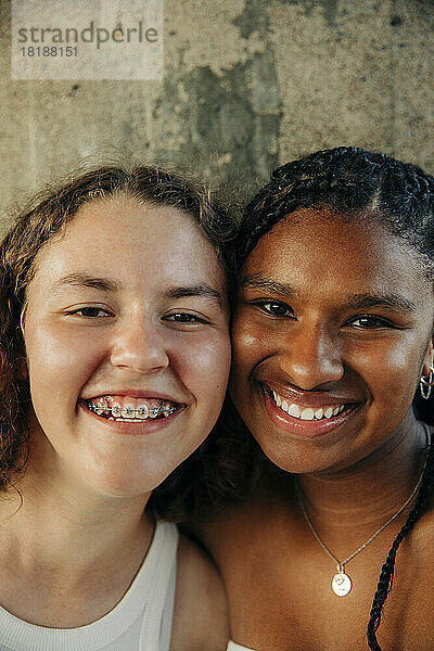 Glückliches Teenager-Mädchen  das eine Zahnspange trägt  mit einer Freundin an der Wand