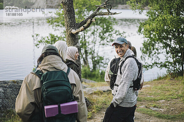Glücklicher Mann mit Hand in der Tasche beim Wandern mit Freunden im Wald