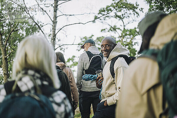 Porträt eines lächelnden Mannes mit Kapuzenhemd beim Wandern mit Freunden im Wald