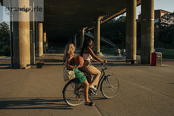 Seitenansicht von Teenager-Mädchen sitzt mit Freund Fahrrad fahren auf der Straße während sonnigen Tag
