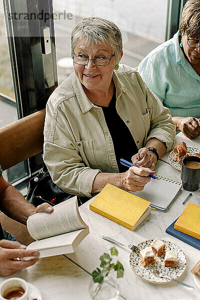Hohe Winkel Ansicht der lächelnden älteren Frau mit Stift und Tagebuch sitzen von weiblichen Freund im Café