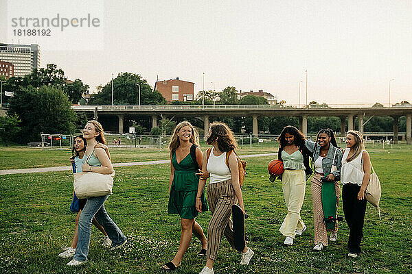 Lächelnde Teenager-Mädchen im Gespräch miteinander beim Spaziergang im Park bei Sonnenuntergang
