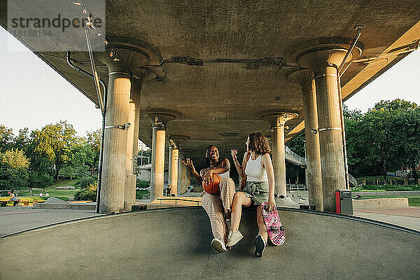 Fröhliche Teenager-Mädchen mit Basketball und Skateboard genießen unter Brücke