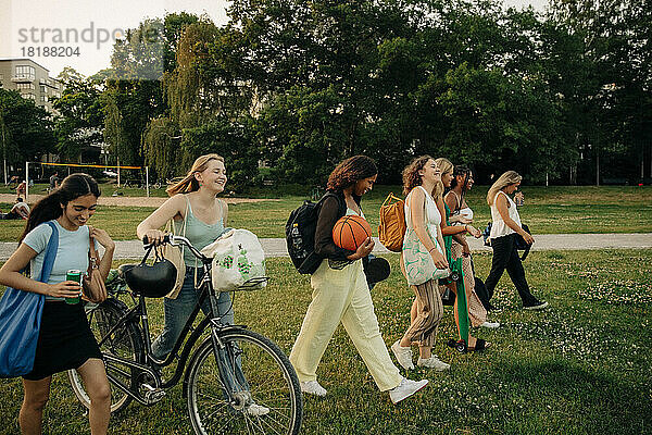 Lächelnde Teenager-Mädchen spazieren zusammen im Park bei Sonnenuntergang