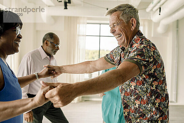 Fröhlicher älterer Mann hält die Hände einer Frau beim Tanzen im Unterricht