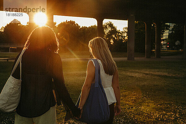 Teenager-Mädchen halten sich an den Händen  während sie im Park bei Sonnenuntergang spazieren gehen