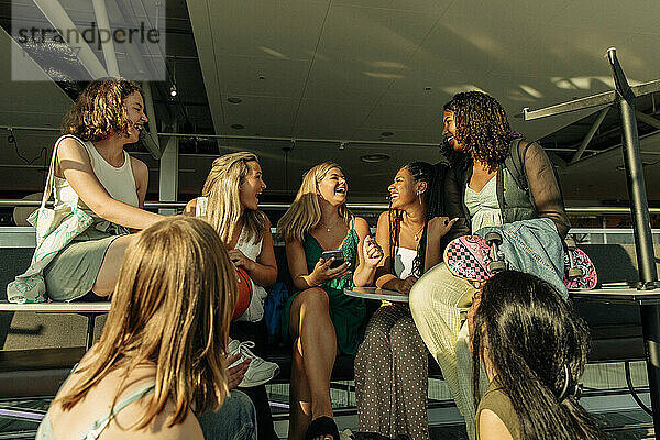 Fröhliche Teenager-Mädchen im Gespräch miteinander  während sie an einem sonnigen Tag vor einem Einkaufszentrum sitzen