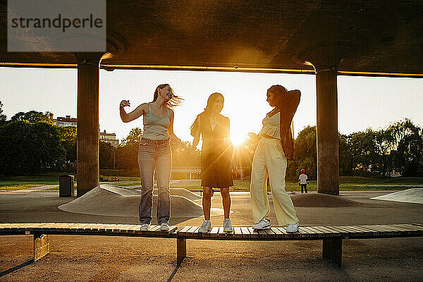 Happy Teenager-Mädchen tanzen auf der Bank  während unter der Brücke bei Sonnenuntergang genießen