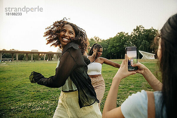 Teenager-Mädchen fotografiert glückliche Freundinnen  die im Park tanzen
