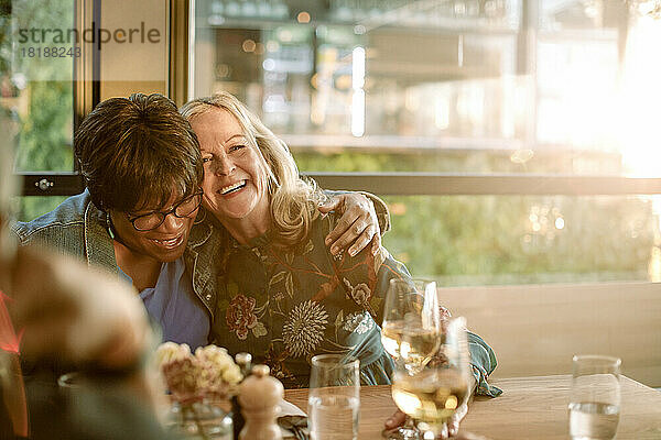 Lächelnde ältere Frau mit Arm um fröhlichen Freund genießt im Restaurant