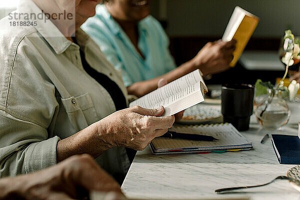 Mittelteil einer älteren Frau  die ein Buch liest  während sie mit ihrer Freundin in einem Café sitzt