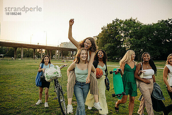 Glückliches Mädchen im Teenageralter  das seine Freundin im Park huckepack nimmt