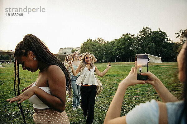 Teenager-Mädchen fotografiert Freundinnen  die im Park bei Sonnenuntergang tanzen