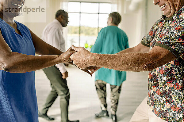 Mittelteil eines glücklichen älteren Paares  das sich an den Händen hält  während es einen Tanz im Unterricht übt