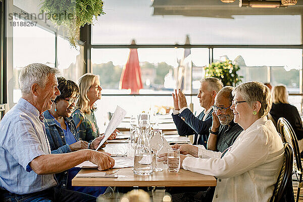 Glückliche ältere Männer und Frauen im Gespräch miteinander  während sie zusammen am Tisch im Restaurant sitzen