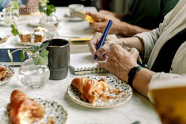 Hände einer älteren Frau  die in einem Café Tagebuch schreibt
