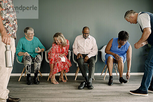 Ältere Frauen und Männer  die Schuhe tragen  während sie auf den Stühlen ihrer männlichen Freunde im Tanzkurs sitzen