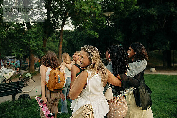 Lächelndes blondes Teenager-Mädchen geht mit Freundinnen im Park spazieren