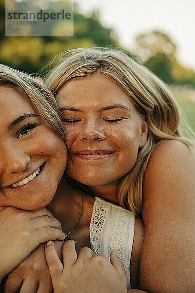 Lächelndes Mädchen mit geschlossenen Augen  das eine blonde Freundin umarmt
