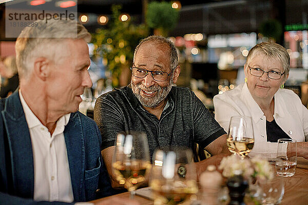Lächelnder älterer Mann im Gespräch mit einem männlichen Freund  während er neben einer Frau im Restaurant sitzt