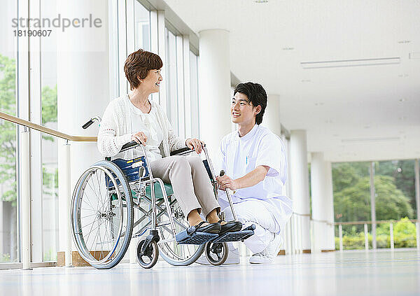 Eine ältere Japanerin im Rollstuhl und ein junger Krankenpfleger unterhalten sich auf dem Flur