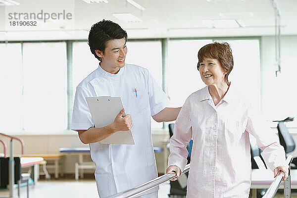 Lächelnde ältere Japanerin und junger Krankenpfleger in der Reha-Einrichtung