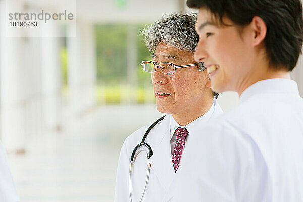 Japanischer Arzt und lächelnder junger Krankenpfleger im Flur