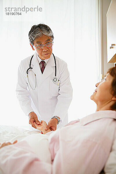 Japanische ältere Frau wird von einem Arzt in einem Krankenzimmer untersucht