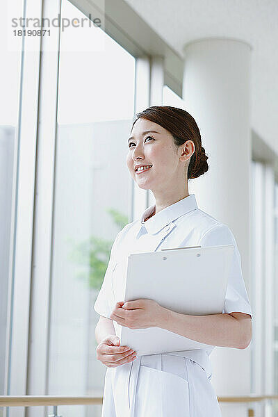 Lächelnde junge japanische Krankenschwester im Flur