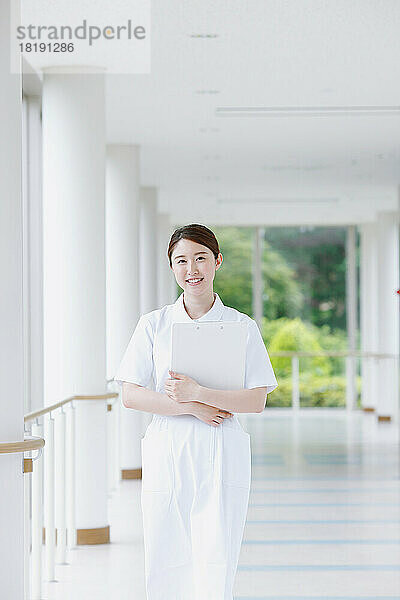 Lächelnde junge japanische Krankenschwester  die durch den Flur geht