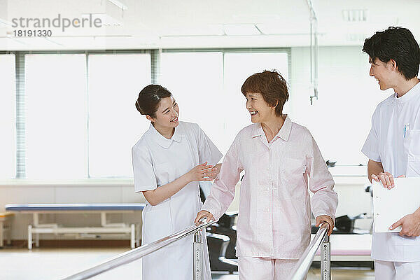 Lächelnde japanische Seniorin und junge Krankenschwestern in der Reha-Einrichtung