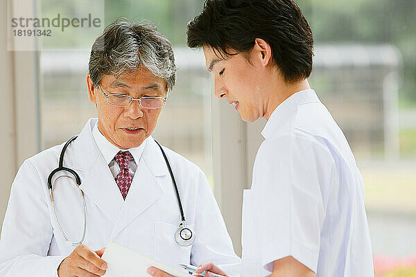 Ein japanischer Arzt und ein junger Krankenpfleger unterhalten sich im Flur