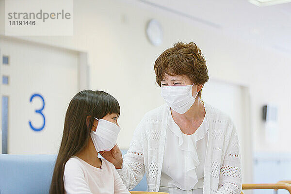 Japanische Seniorin und Enkelkind in Masken im Wartezimmer des Krankenhauses