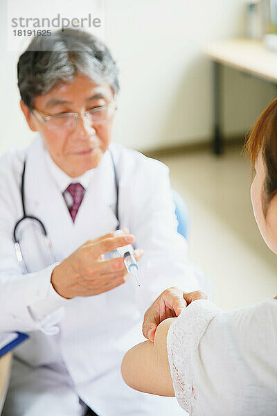 Japanischer Arzt gibt einem Patienten eine Injektion