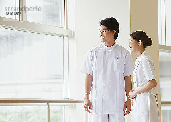 Lächelnde junge japanische Krankenschwester bei einem Gespräch im Flur
