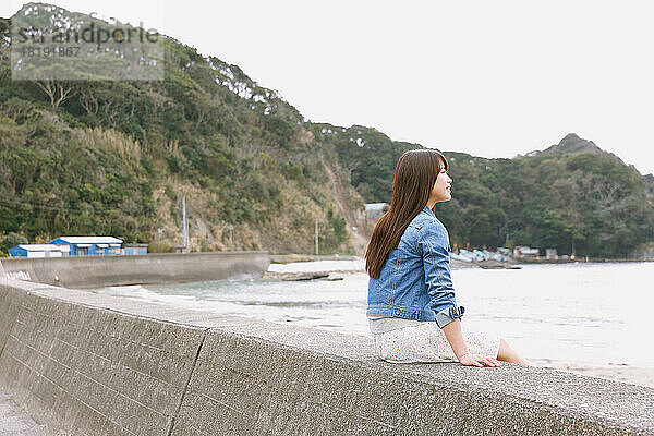 Junge Japanerin sitzt auf der Meeresbarriere